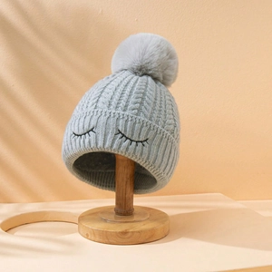 Berretto in maglia con occhi ricamati e grande pompon su supporto in legno