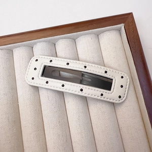 Detailed close-up of white PU leather BB clip with black polka dots on velvet tray