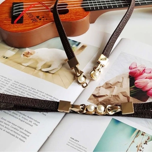 Detail of slim woven dark brown belt featuring gold metal buckle with pearl inlay
