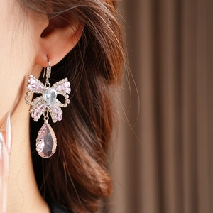 Close-up of pink zircon bow earring with a teardrop tassel pendant worn by a model
