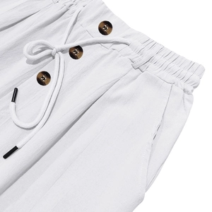 Close-up of white linen trousers featuring a drawstring waist and vintage brown buttons