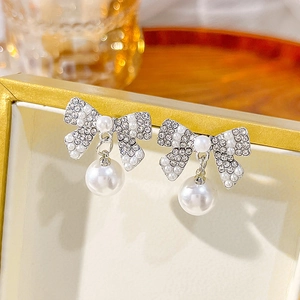 Macro detail of bowknot earrings with crystal inlay and a large hanging white pearl