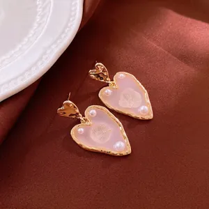 Gold plated heart drop earrings with pink resin and pearl accents on silk fabric