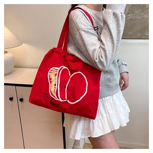 Detail view of red canvas tote bag with apple print worn by a model in casual style