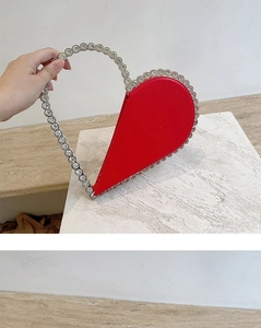 Macro shot of red patent leather heart-shaped clutch with rhinestone trim and beaded handle