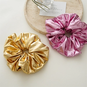 Metallic gold and pink oversized scrunchies with shiny reflective fabric on beige surface