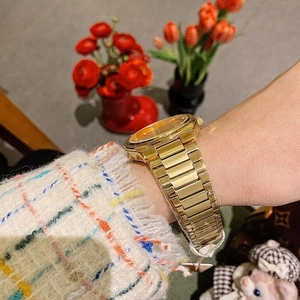 Close-up of golden steel strap watch with vibrant orange dial on a female wrist