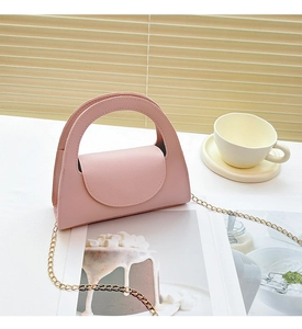 Pink PU leather handbag with gold chain strap placed on magazine near coffee cup