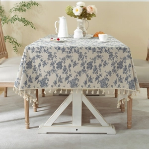 Rectangle beige linen tablecloth with blue floral patterns and tassel fringe in a cozy room