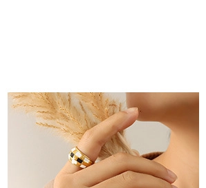 Vue détaillée d'une bague à damier dorée portée au doigt sur un fond minimaliste et épuré