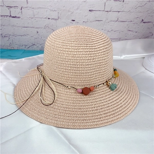 Detail of beige straw sun hat featuring colorful beads and decorative floral pendant charms