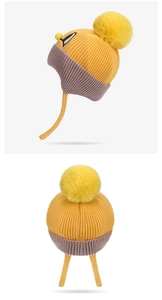 Detail of winter knit baby hat with yellow pompom, earflaps, and colorful patchwork