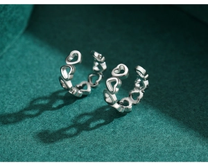 Detailed view of silver heart-shaped ear cuffs on green textured fabric with heart shadows