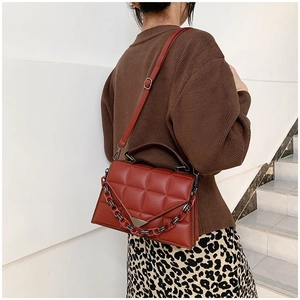 Detail of reddish brown quilted crossbody bag with chunky chain strap on a model