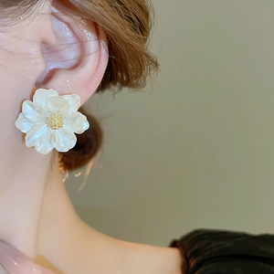 Detailed close-up of a white resin camellia earring with a gold center on a model