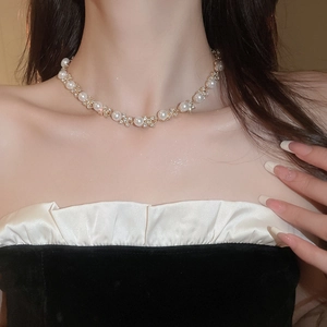 Dettaglio della collana dorata con perle bianche e accenti floreali in zircone lucido