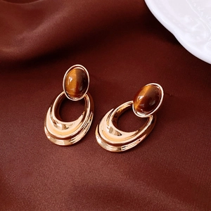 Detail of 18K gold plated oval earrings with tiger eye stone on brown satin fabric