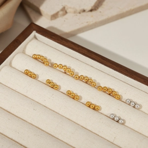 Minimalist geometric gold and silver beaded drop earrings displayed on a luxury jewelry tray
