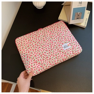 Floral laptop sleeve with pink flowers and a white quote label on a wooden desk