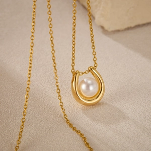 Elegant U-shaped gold titanium necklace with white pearl on minimalist stone background