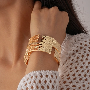 Macro detail of wide gold hammered cuff bracelet with irregular geometric cutouts on wrist