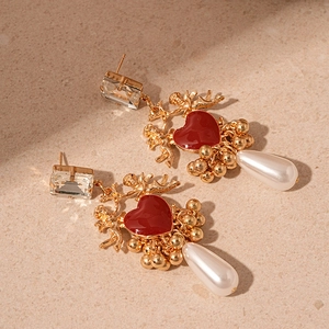 Gros plan sur des boucles d'oreilles baroques cœur en émail rouge et détails de Cupidon