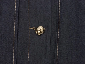 Détail du denim bleu foncé avec bouton noeud doré et coutures jaunes contrastées