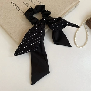 Detailed view of elegant black polka dot hair scrunchie with long ribbons on vintage book