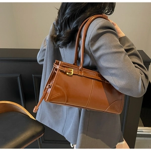Brown leather tote bag with buckle detail shown on a grey blazer outfit styling