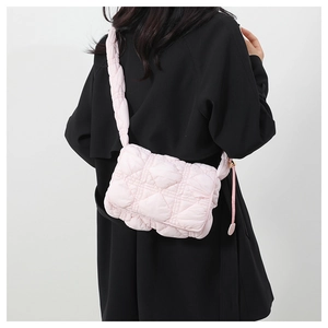 Quilted light pink crossbody bag with padded strap shown on model over a black coat