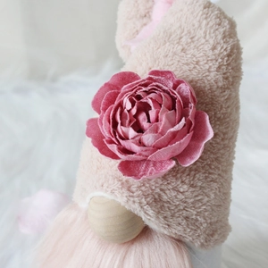 Close-up of a plush gnome featuring a beige furry hat, pink fabric flower, and long beard