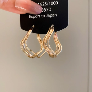Detailed close-up of 925 silver wavy gold hoop earrings held against a neutral background
