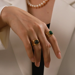 Close-up of gold leaf-textured wide band rings with green gemstones on model hand