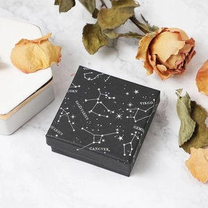 Square black jewelry box with white zodiac constellation patterns on marble background