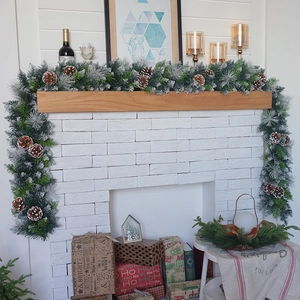 Detailed view of snowy Christmas garland with pine cones on a festive white fireplace
