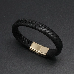 Detail of black braided leather bracelet with magnetic golden metal clasp on gray surface