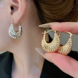 Macro detail of golden metallic hoop earring featuring a unique wrinkled texture design