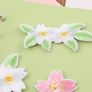Embroidered cartoon flower patches in pink and white with green leaves on light background
