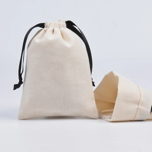 Detail of beige cotton drawstring jewelry pouch showing silver ring storage on white background