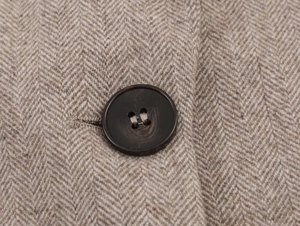 Macro shot of brown herringbone wool fabric and a dark resin button on a blazer