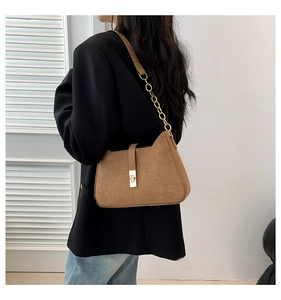 Detail of a brown suede shoulder bag featuring a gold chain strap and square metal lock