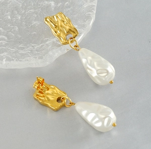 Detailed macro view of irregular gold metal plate and white teardrop pearl earrings