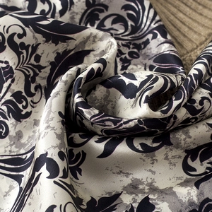 Grey silk neck scarf with black baroque pattern showing soft fabric texture and drape