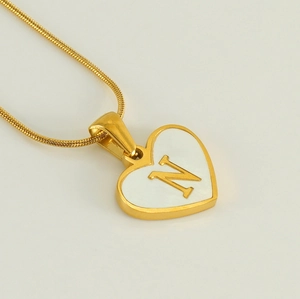 Macro shot of 18K gold heart pendant with white shell inlay and letter N detail