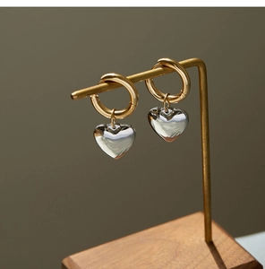 Close-up of heart charm earrings in gold and silver finish on a brass display stand