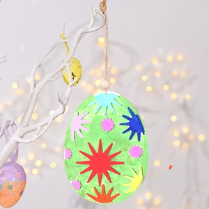 Detail of green Easter egg ornament with colorful stars hanging on a white branch