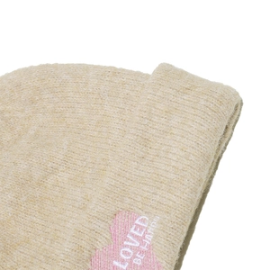 Primer plano del gorro de punto beige con bordado de corazón rosa y texto LOVED BE HAPPY