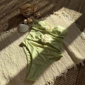 Detail of mint green cutout swimsuit with white 3D rose and side ruching on sand-style mat