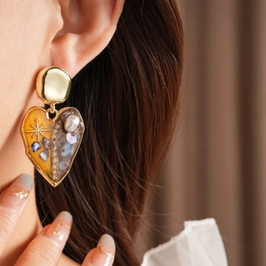 Close-up of heart-shaped pearl earrings with gold metal and orange resin on model