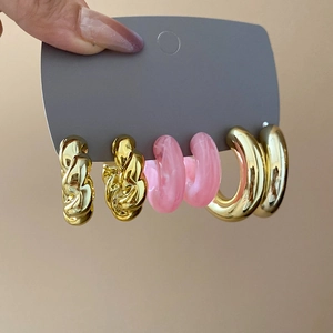 Detailed set of twisted gold metal, pink resin, and chunky hoop earrings on display
